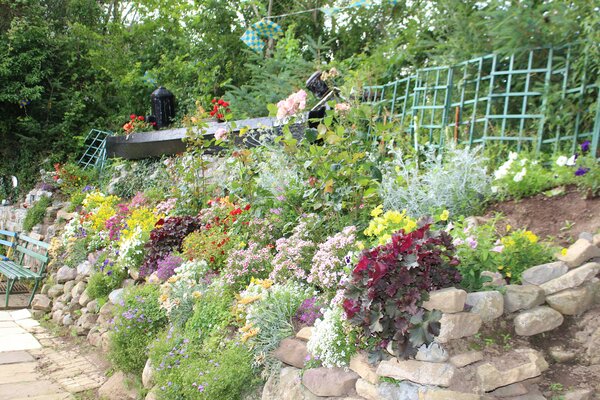 Bunte Gartenlandschaft mit einer Vielzahl von blühenden Pflanzen entlang einer steinernen Mauer.